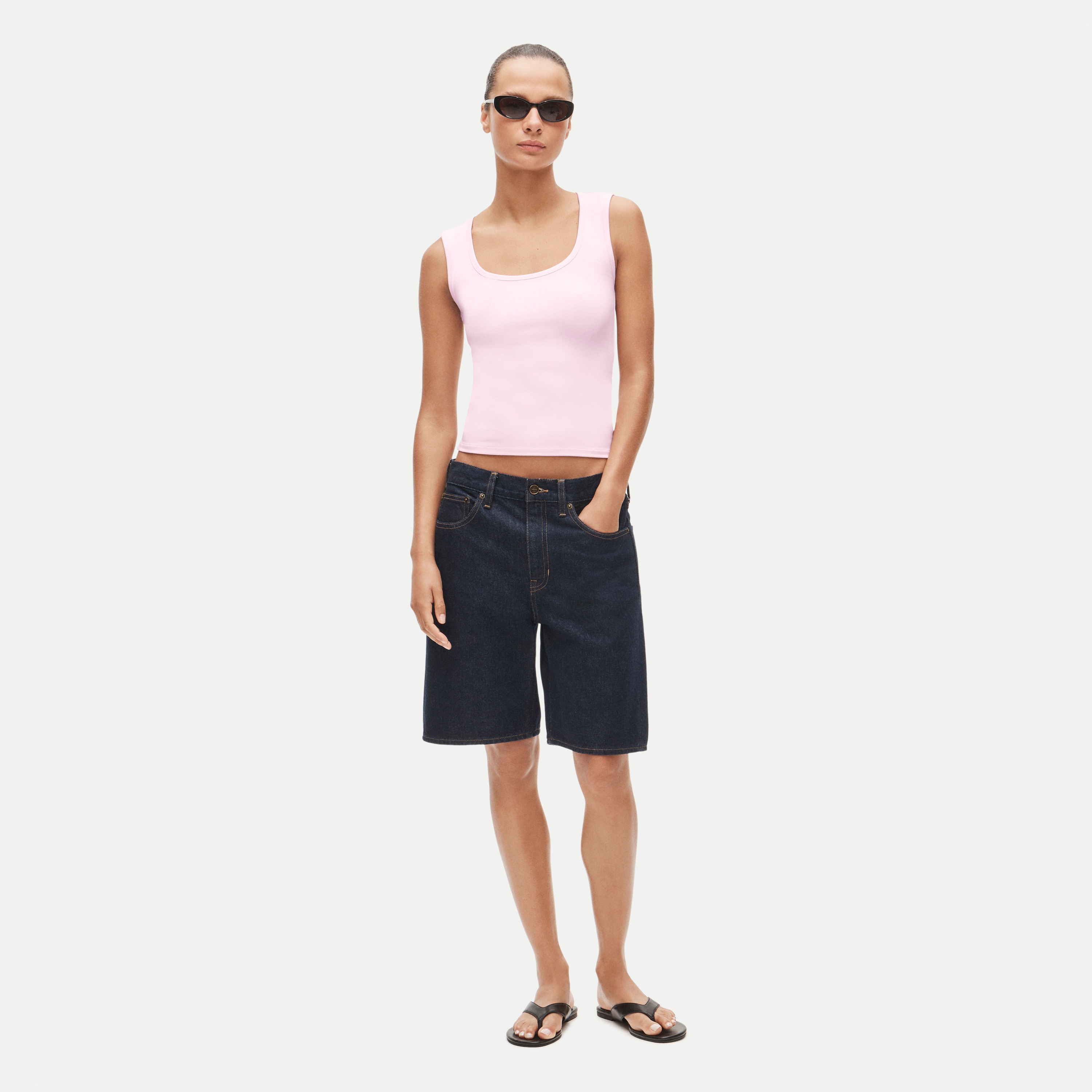 Woman wearing a Pink Refined rib scoopneck tank top paired with dark denim shorts, sunglasses and black sandals.