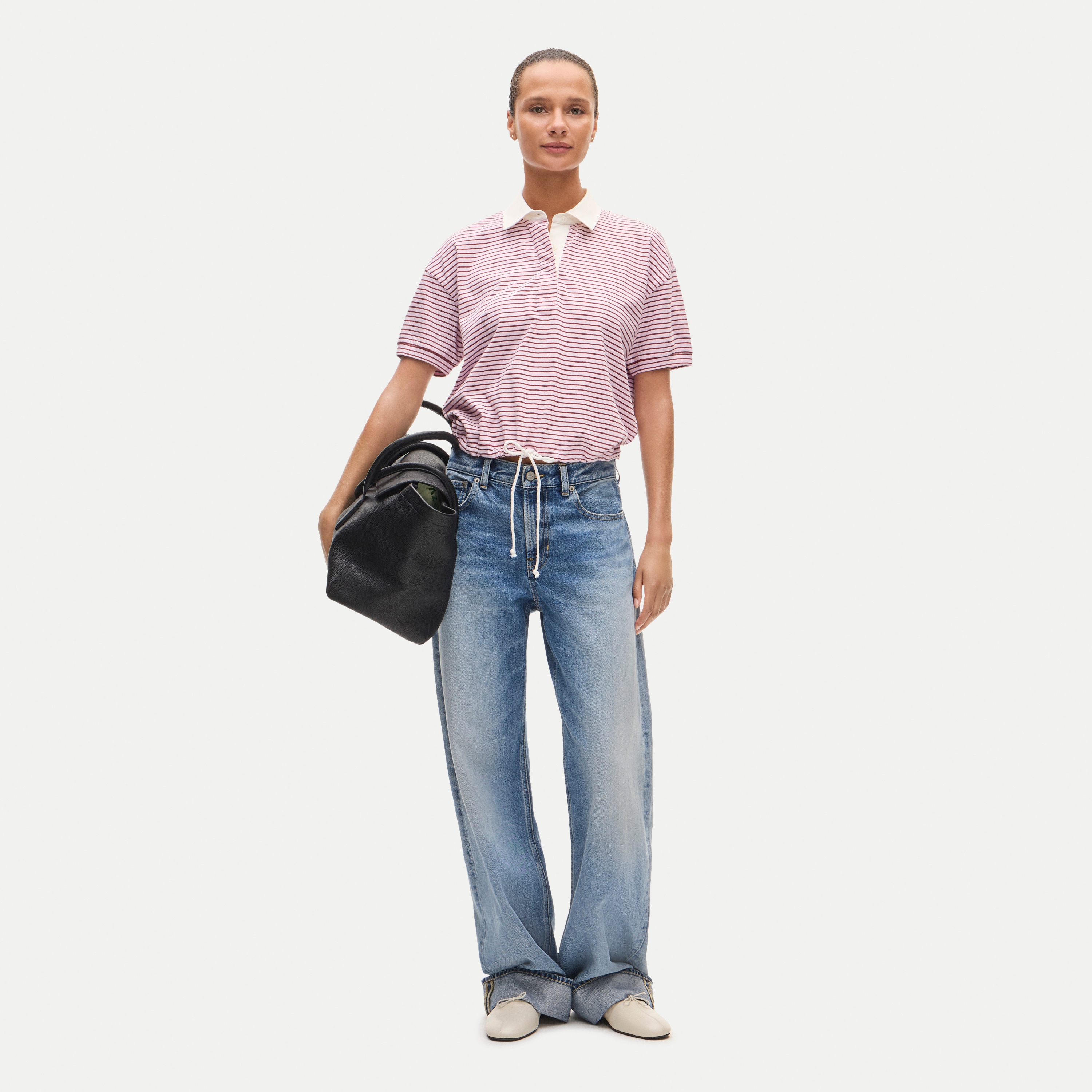 Woman wearing White Boyfriend jersey drawstring-waist polo shirt in stripe paired with blue jeans and a black bag.
